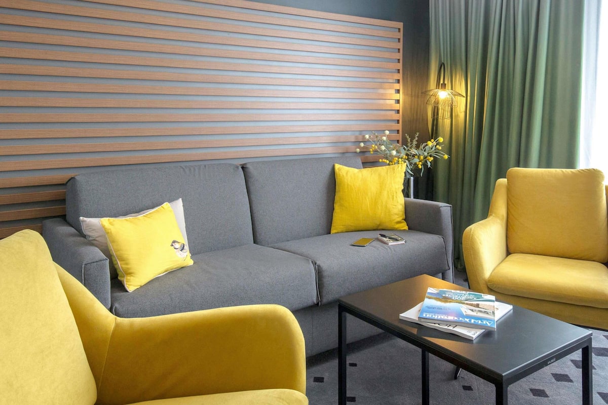 Una sala de estar moderna con un sofá gris, sillones amarillos y una mesa de centro con revistas.