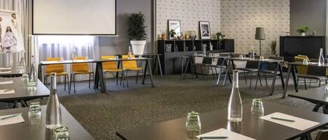 A conference room with tables, chairs, a projector screen, and a large potted plant.