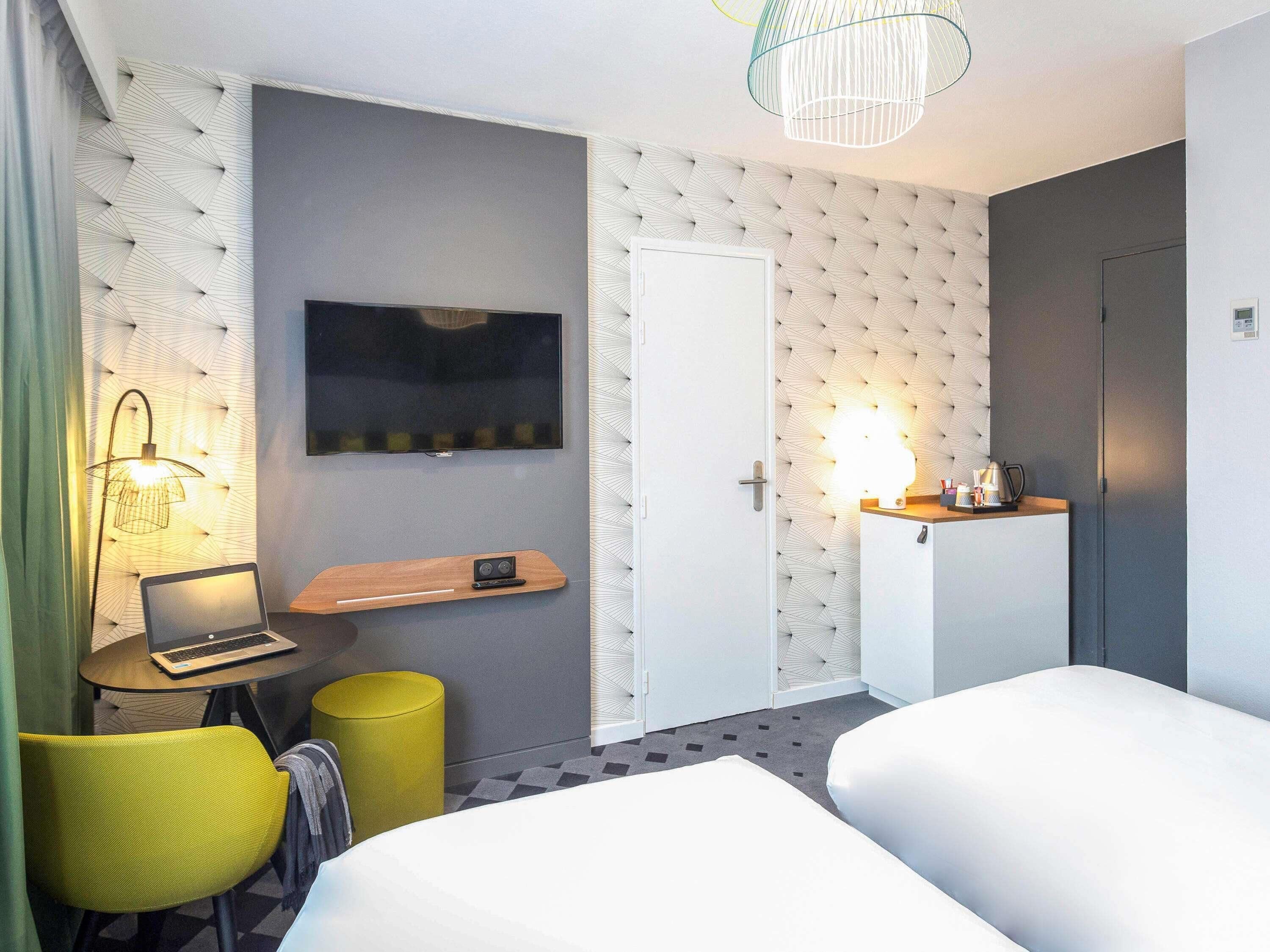 A hotel room with a bed, a desk with a laptop, a TV, a lamp, and a wardrobe.
