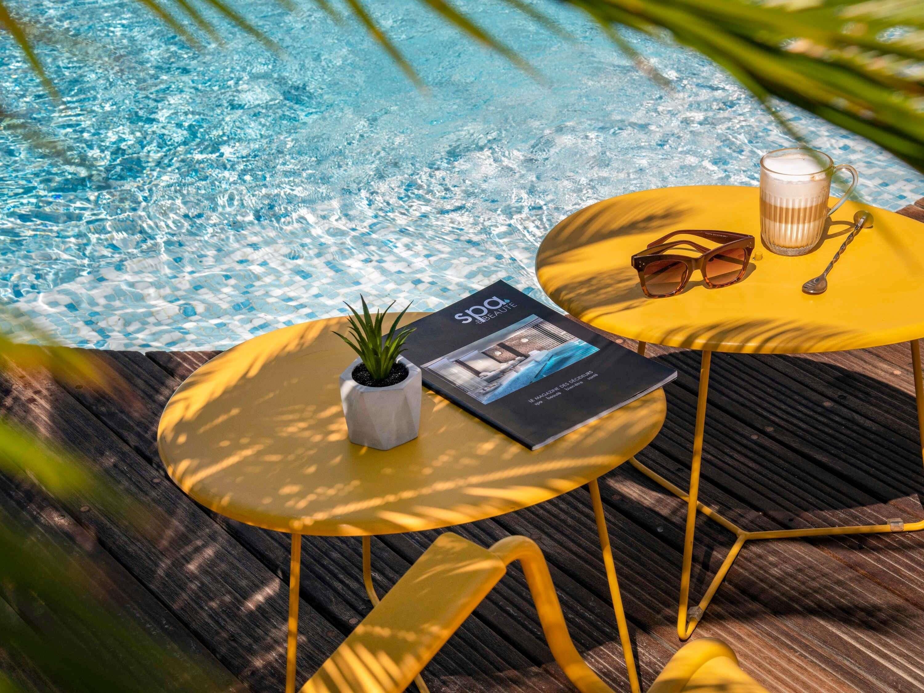 A poolside setting with a magazine, sunglasses, and a candle on yellow tables.
