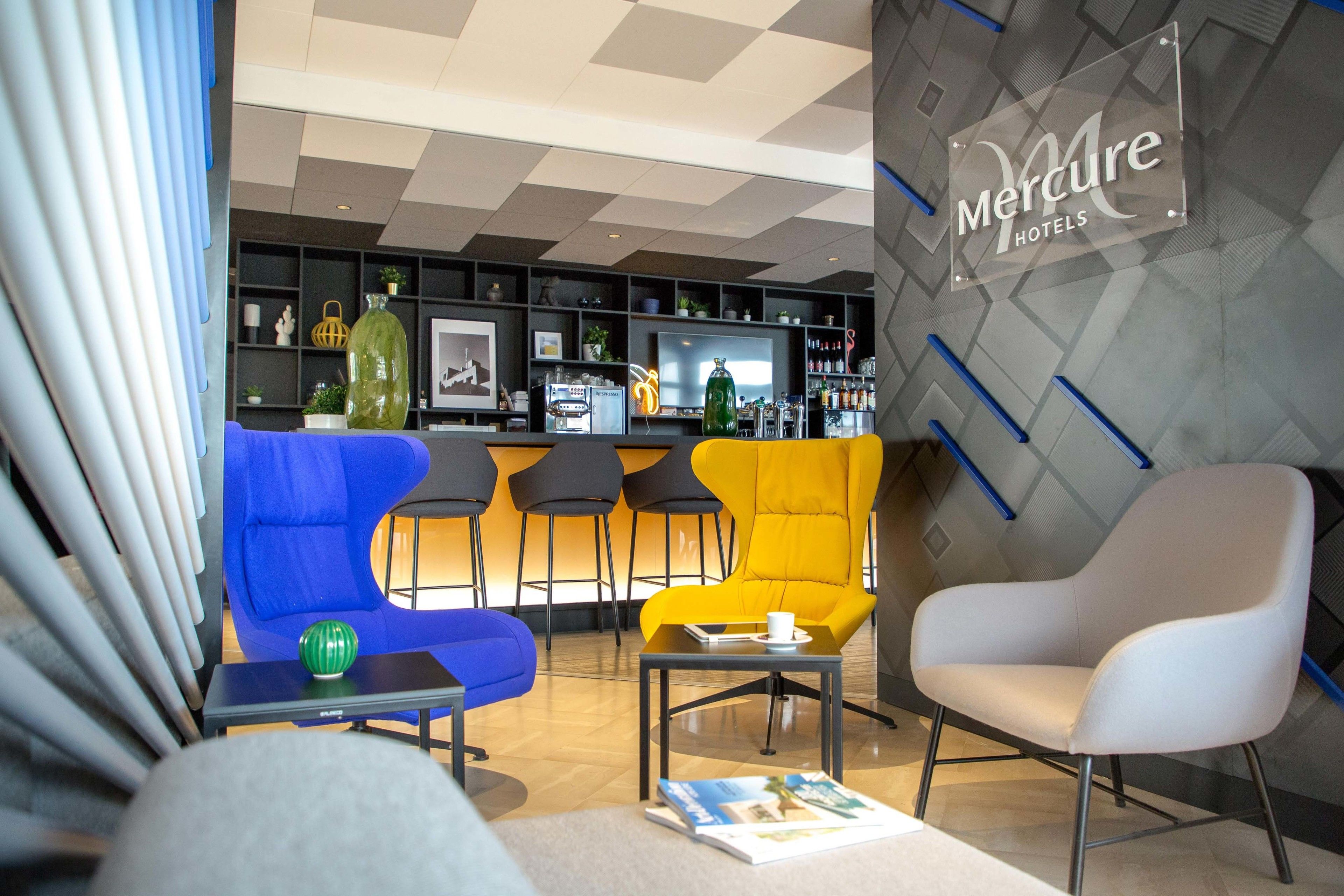 Un moderno vestíbulo de hotel con áreas de descanso, un mostrador de recepción y un bar visible.