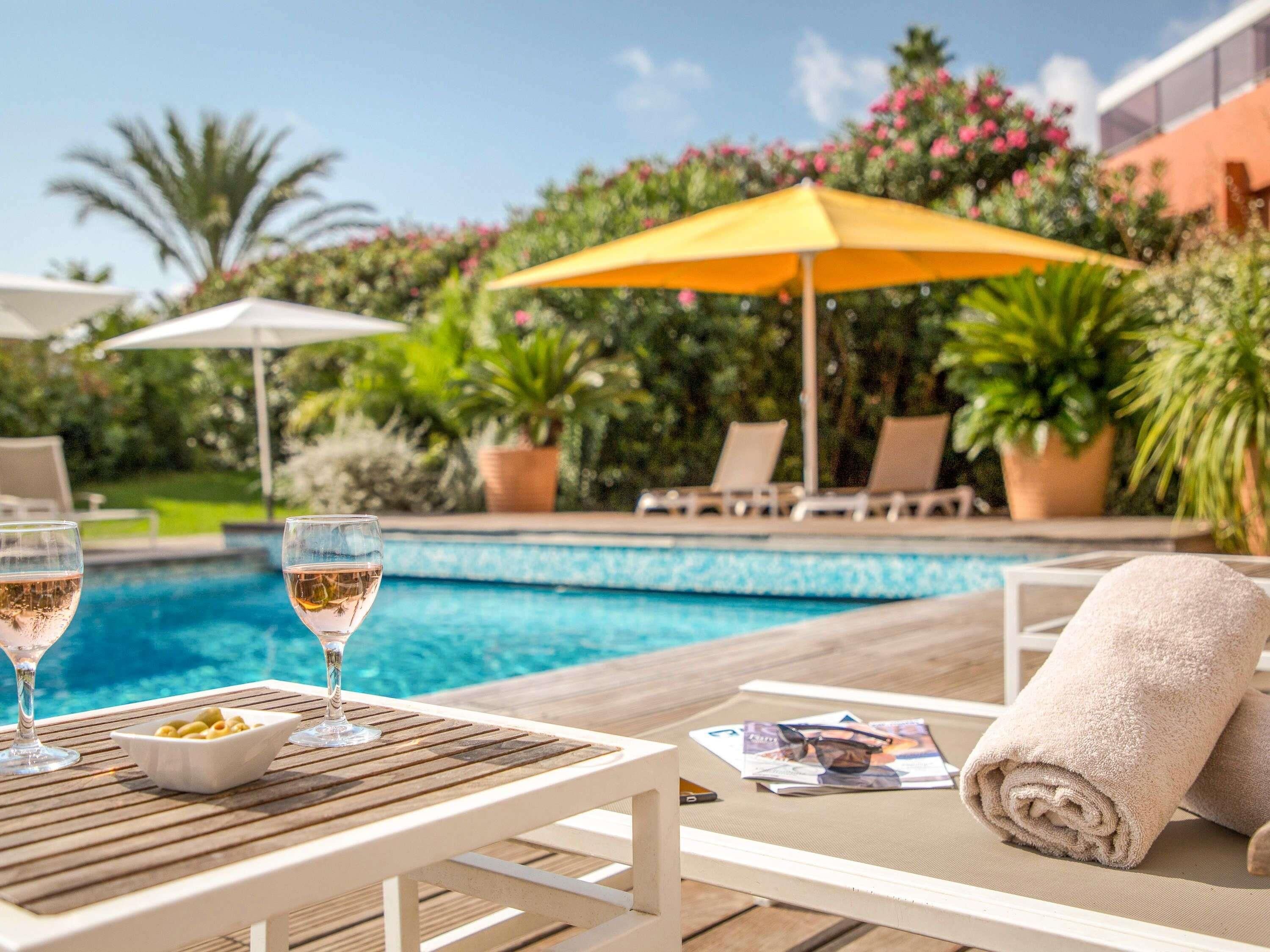 Zona de piscina con dos sillones de descanso, una mesa con bebidas y un tazón de aceitunas, y una sombrilla amarilla.