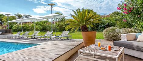 A poolside area with lounge chairs, a table with drinks, and a large potted plant.