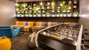 A modern lounge area with a foosball table, sofas, and a wall of potted plants.