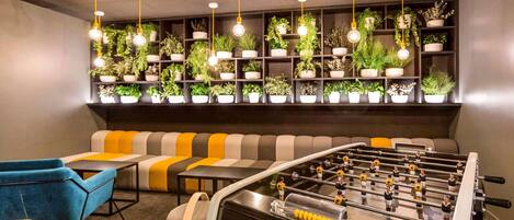 A modern lounge area with a foosball table, sofas, and a wall of potted plants.