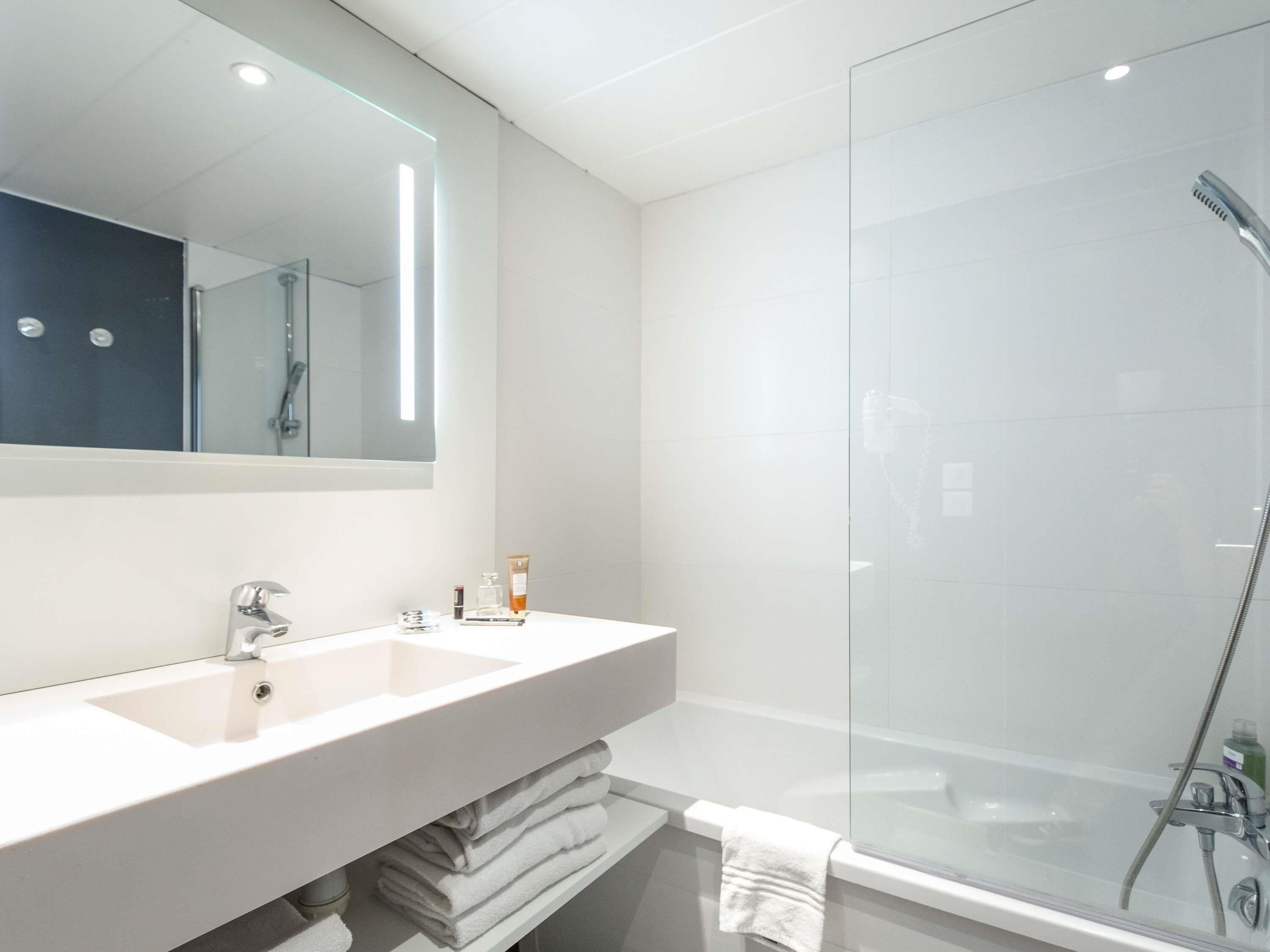 Une salle de bain moderne avec un grand miroir, deux lavabos, une douche en verre et des serviettes soigneusement pliées.