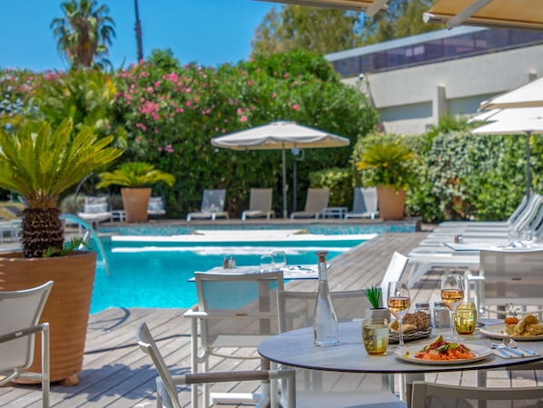 A poolside dining area with tables, chairs, and a pool.