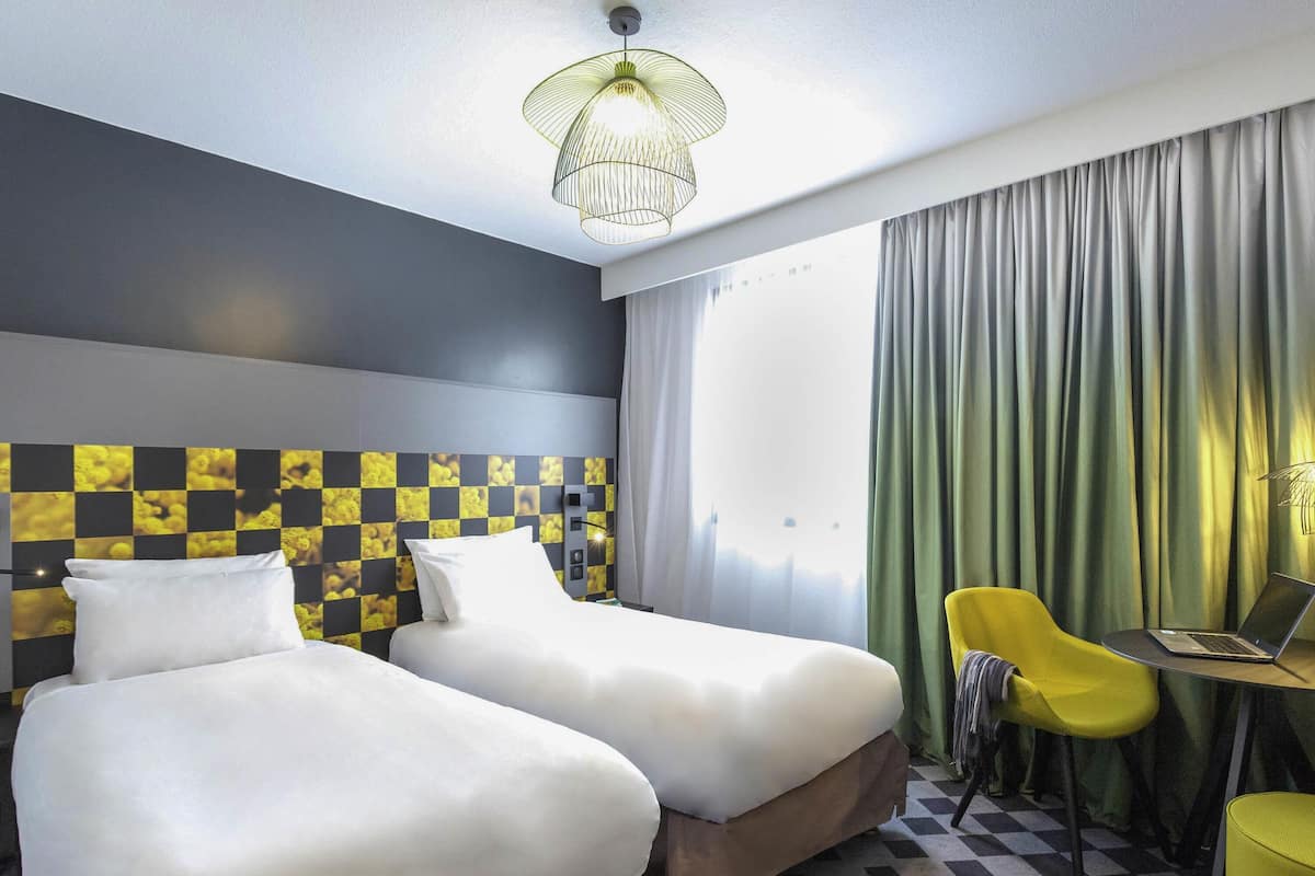 Habitación de hotel con dos camas, un escritorio con una computadora portátil, una silla y piso a cuadros.
