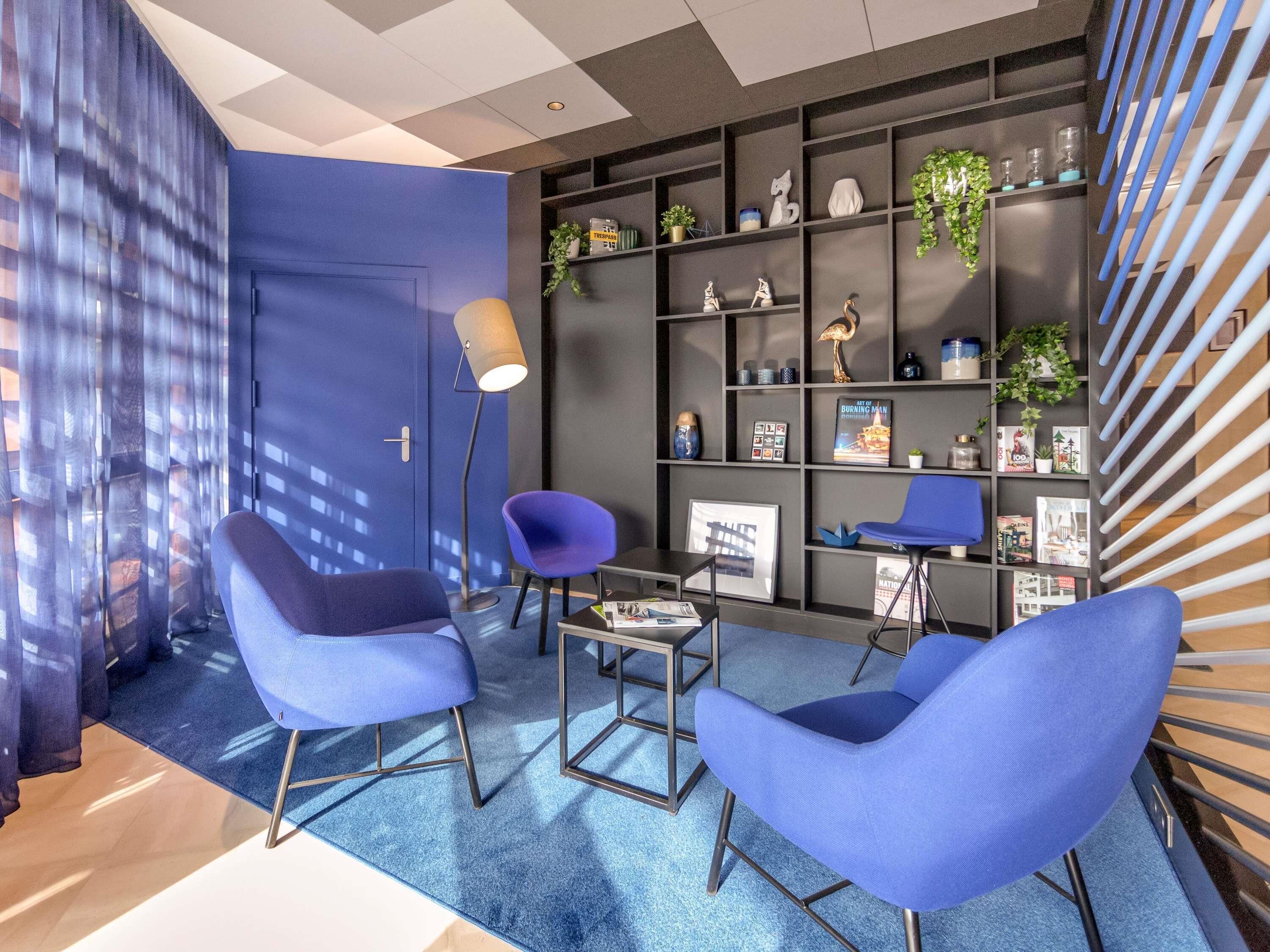 A modern office space with blue chairs, a desk, and a bookshelf with various items.