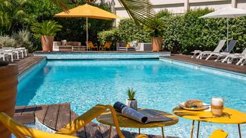 A swimming pool with lounge chairs and umbrellas, surrounded by greenery and a tiled deck.