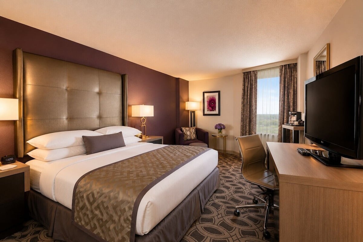 Hotelkamer met een groot bed, een bureau met een televisie, een stoel, een nachtkastje, een lamp en een raam met gordijnen.
