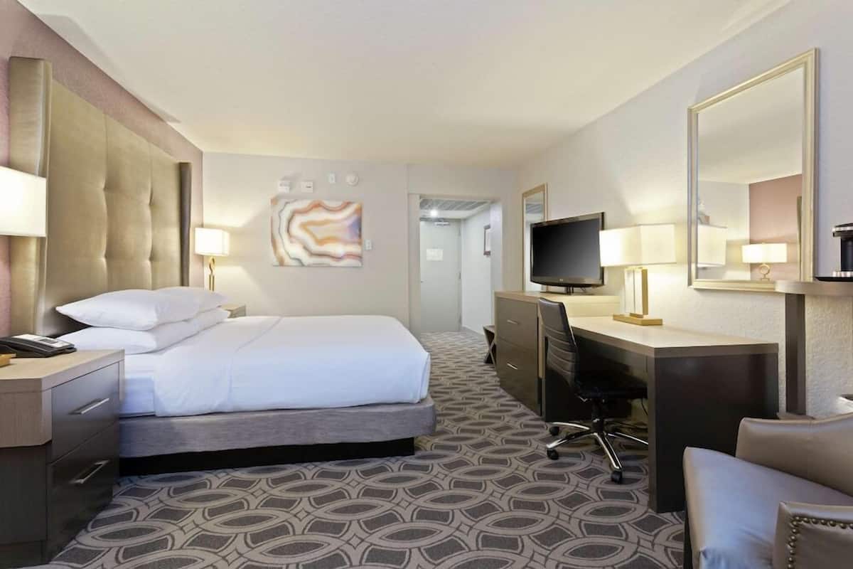 Een hotelkamer met een bed, bureau, stoel, televisie en kunst aan de muur.