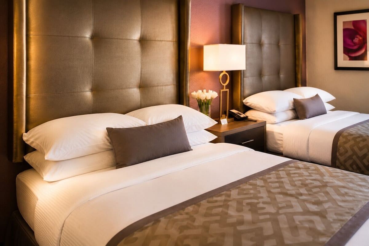 Een hotelkamer met twee bedden, een nachtkastje met een lamp en een lijst aan de muur.