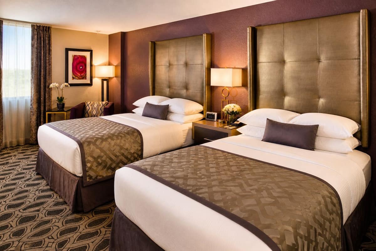 Een hotelkamer met twee bedden, een nachtkastje met lamp, een lijst met afbeelding aan de muur en een kamerbreed tapijt met dessin.