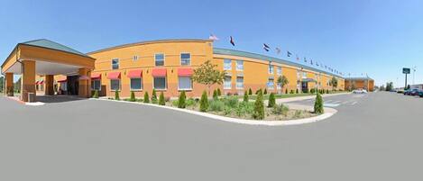 A hotel with a yellow facade, multiple windows, and a covered parking area.