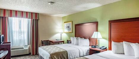 Une chambre d’hôtel avec deux lits, un bureau, une chaise, une lampe et un téléphone.