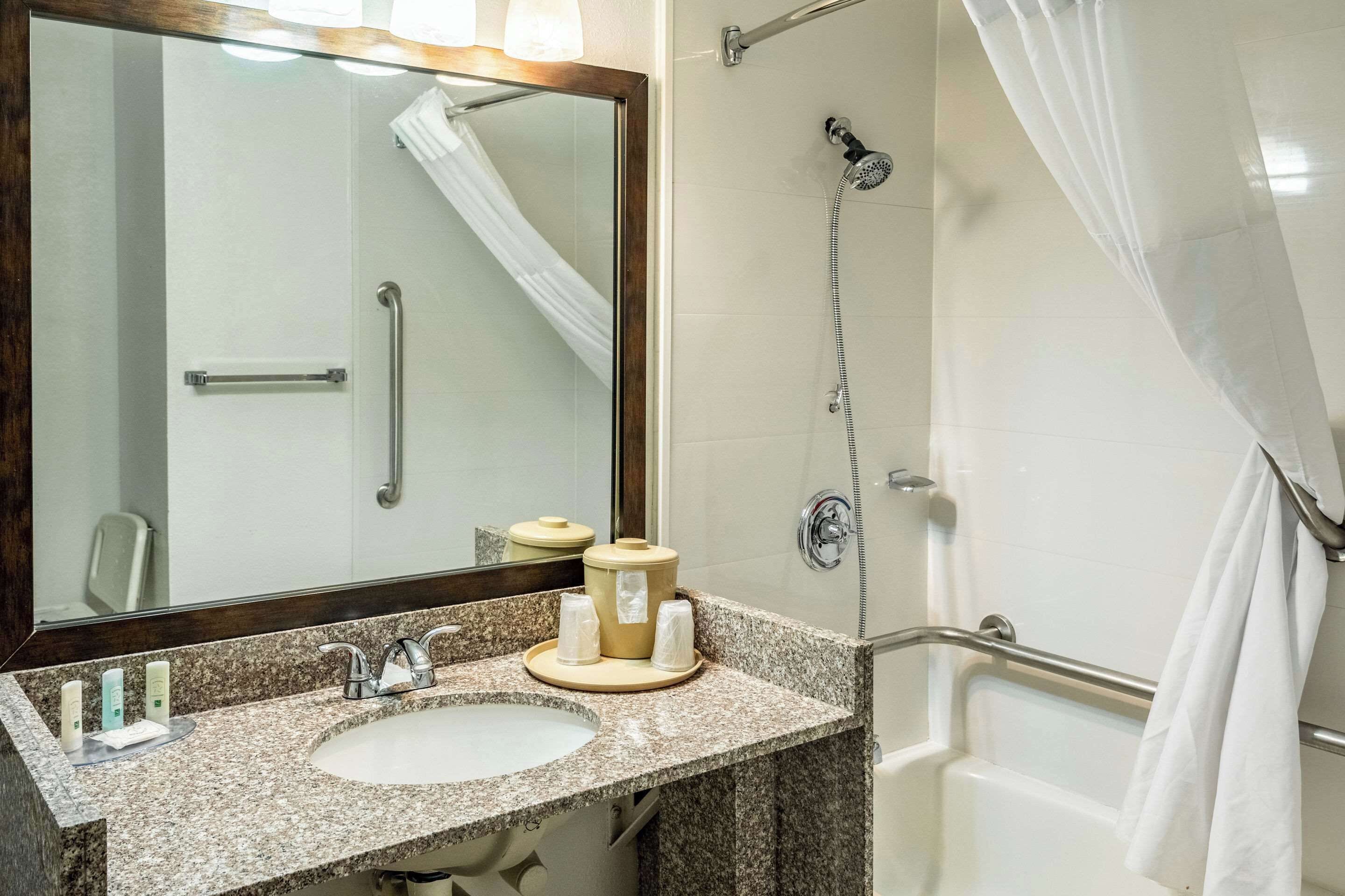 A bathroom with a sink, mirror, shower, and grab bars.