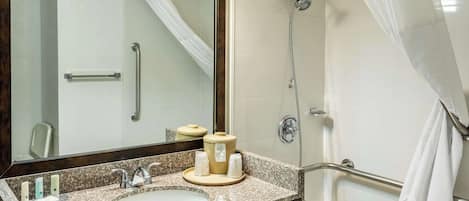 A bathroom with a sink, mirror, shower, and grab bars.