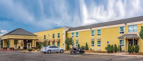 Un hotel con entrada cubierta, aparcamiento y una motocicleta estacionada frente.