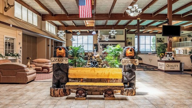 Un hall d’entrée spacieux avec un banc en bois et deux statues d’ours portant des panneaux « Bienvenue », un grand drapeau américain et une enseigne « Quality Inn ».