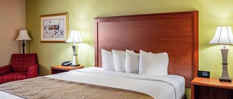 A hotel room with a large bed, two bedside tables with lamps, a red chair, and a framed picture on the wall.