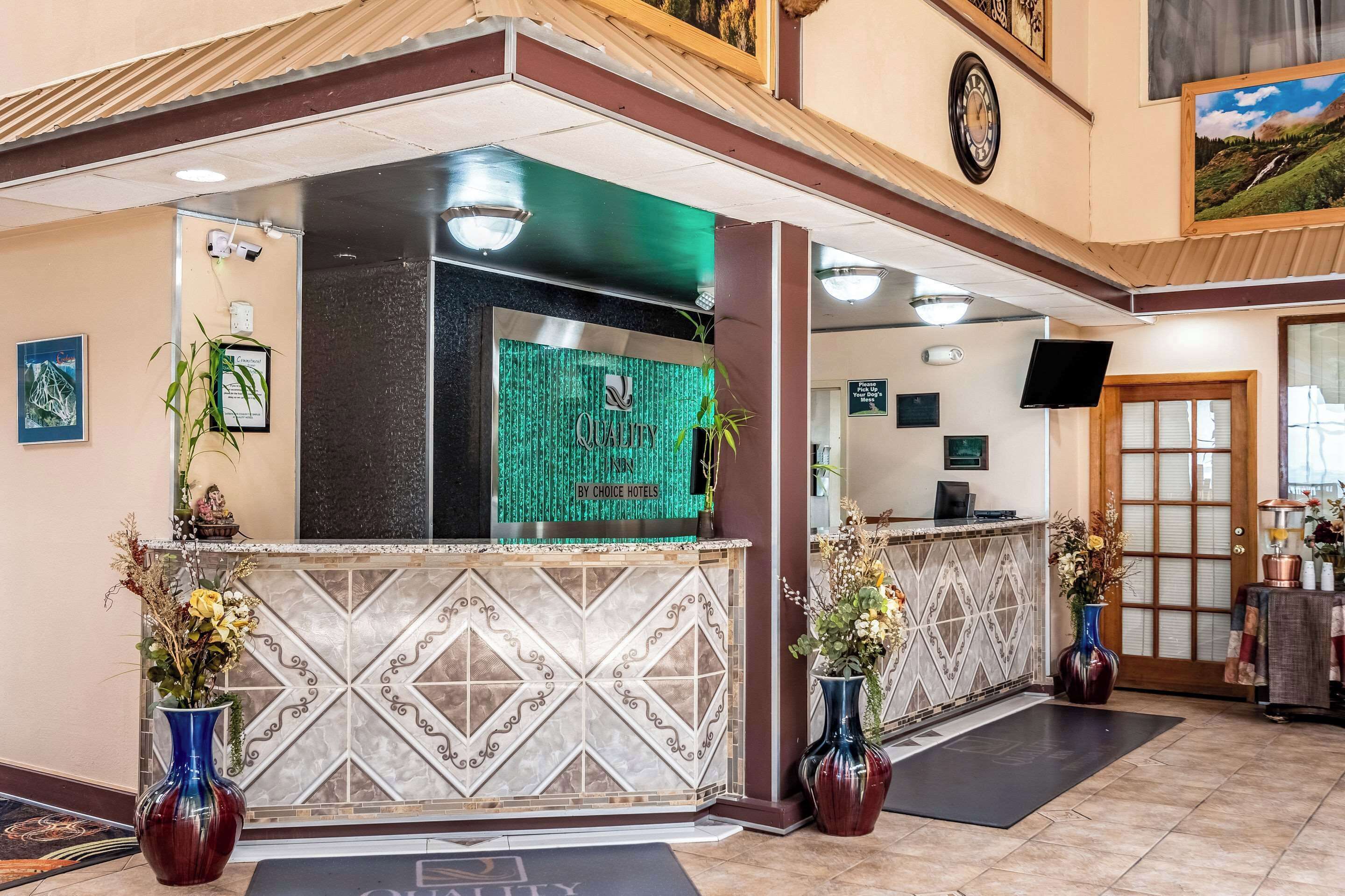 Zona de recepción de un hotel con diseño moderno, que incluye un mostrador de recepción, jarrones decorativos y un reloj en la pared.