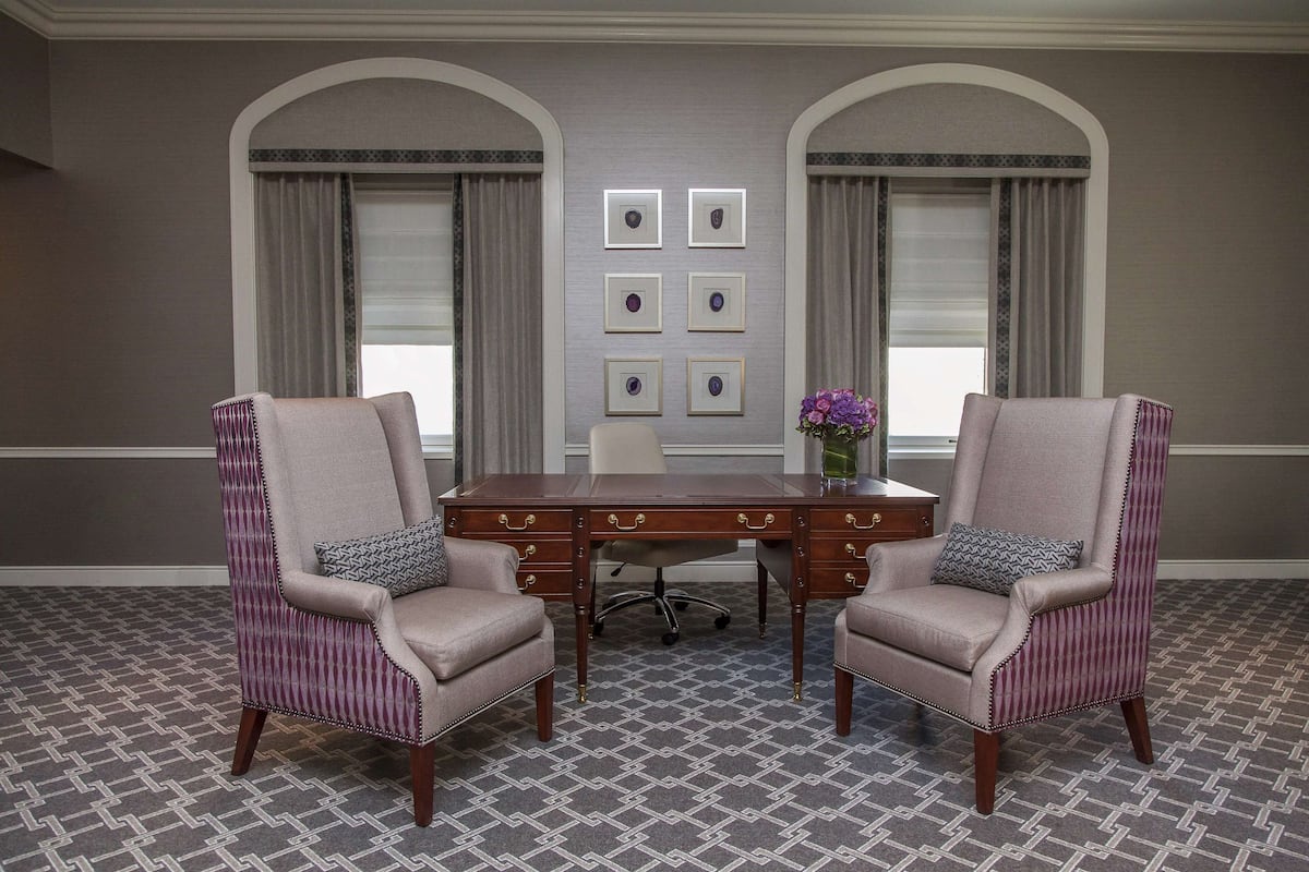 A conference room with a wooden table, two upholstered chairs, a vase with flowers, and framed pictures on the wall.