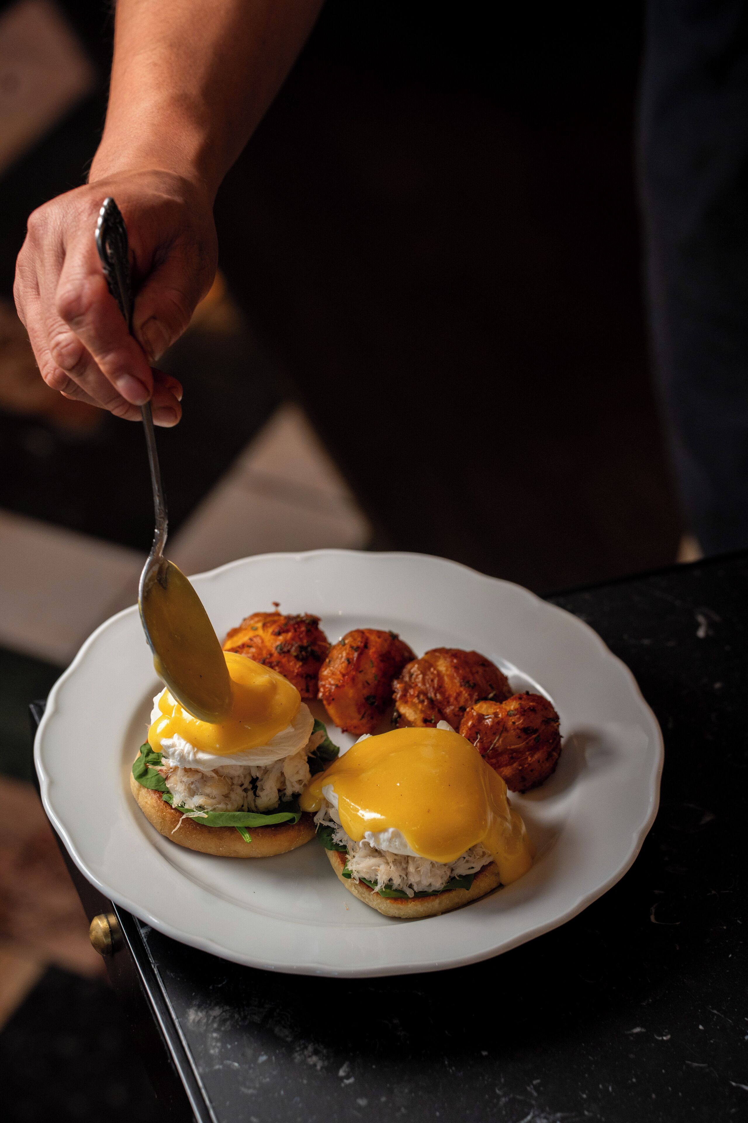 A plate with two eggs benedict sandwiches and two meatballs.