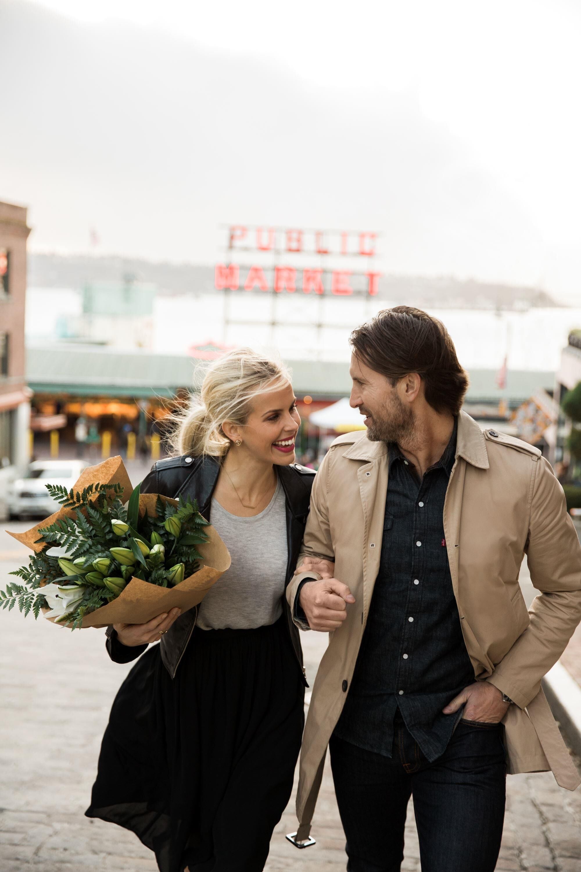 A couple walking on a street with a 'PUBLIC MARKET' sign in the background.