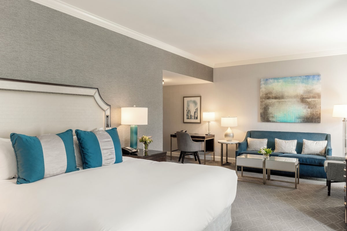 A hotel room with a large bed, a desk, a chair, a sofa, and two lamps.