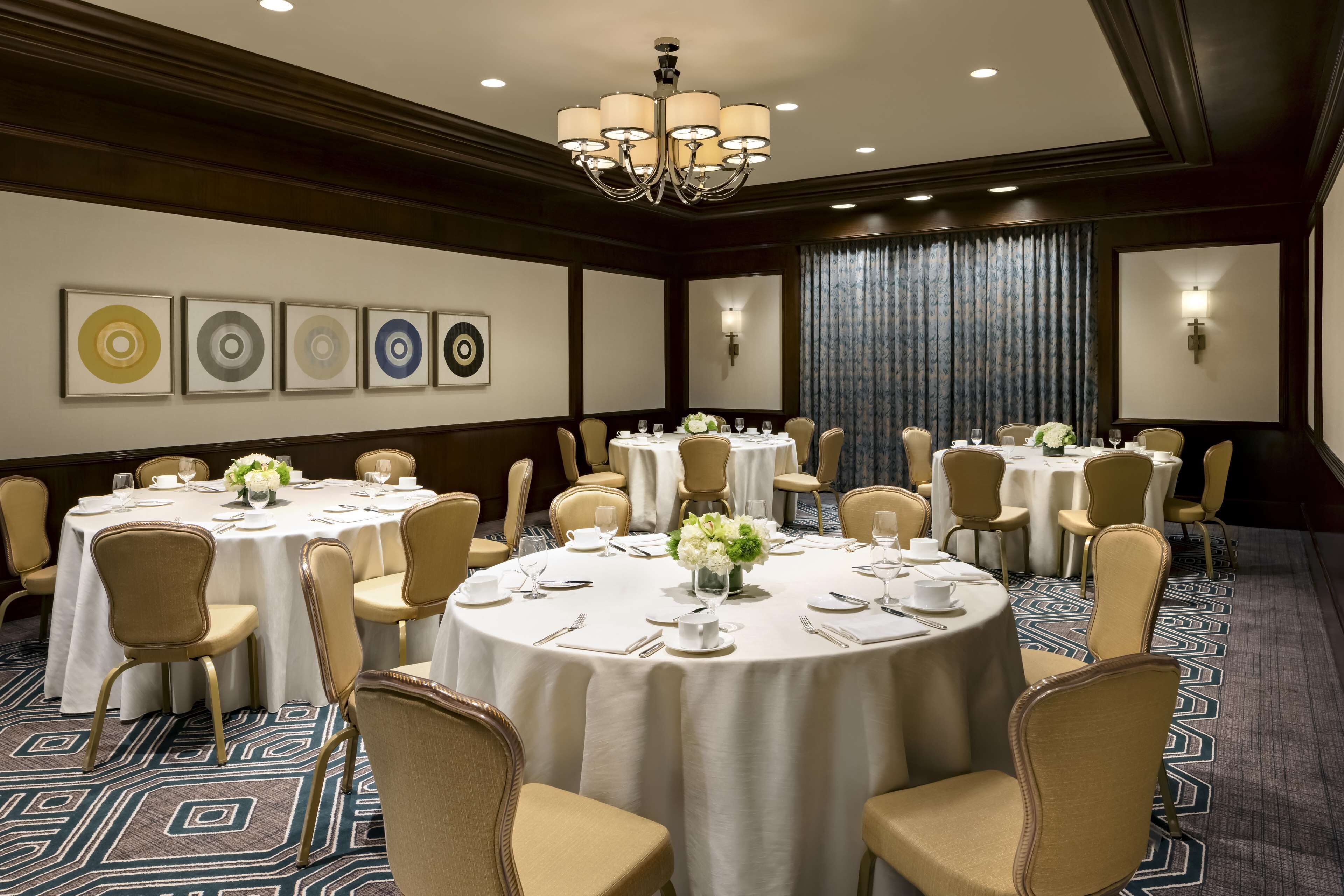 A conference room with round tables, beige chairs, and a chandelier.