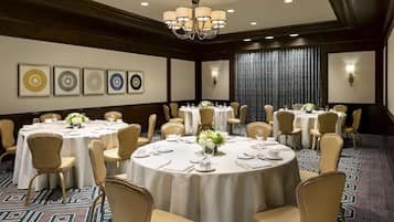 A conference room with round tables, beige chairs, and a chandelier.