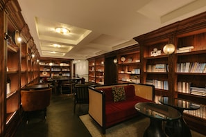 Cozy library with a classic design, featuring a central sofa, glass-top tables, and wooden bookshelves.