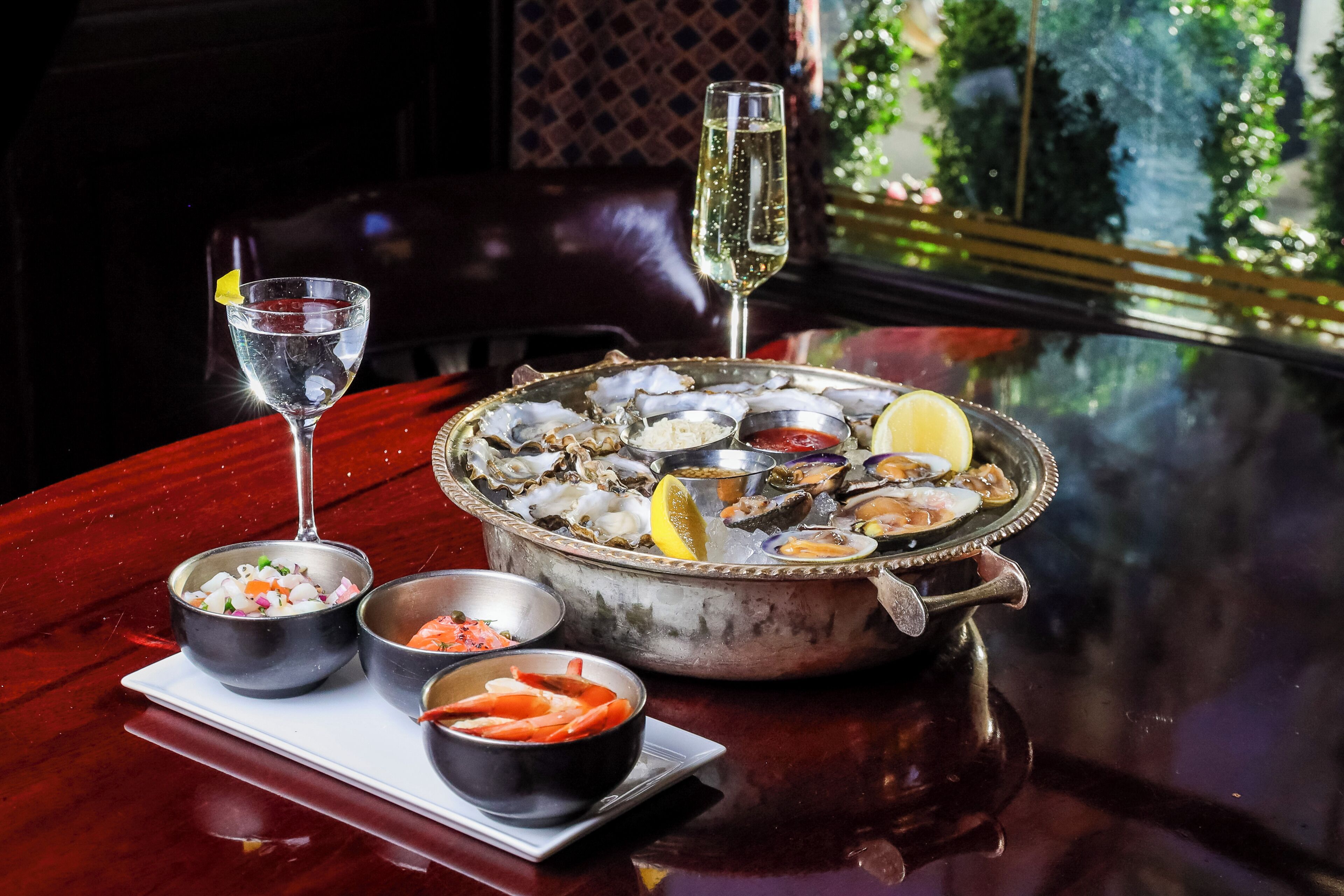 Una bandeja de mariscos con ostras, camarones y limón sobre una mesa con una copa de champán.