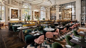 Un restaurant spacieux avec de hauts plafonds, de magnifiques lustres et différents types de sièges, notamment des banquettes et des tables.