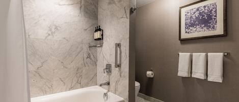 Une salle de bain moderne avec une baignoire, une douche, des murs en marbre et une œuvre d’art encadrée accrochée au mur.