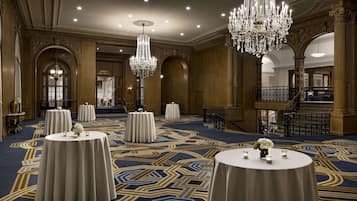 Un salón de baile elegante con candelabros ornamentados, una alfombra estampada y varias mesas redondas preparadas para eventos.