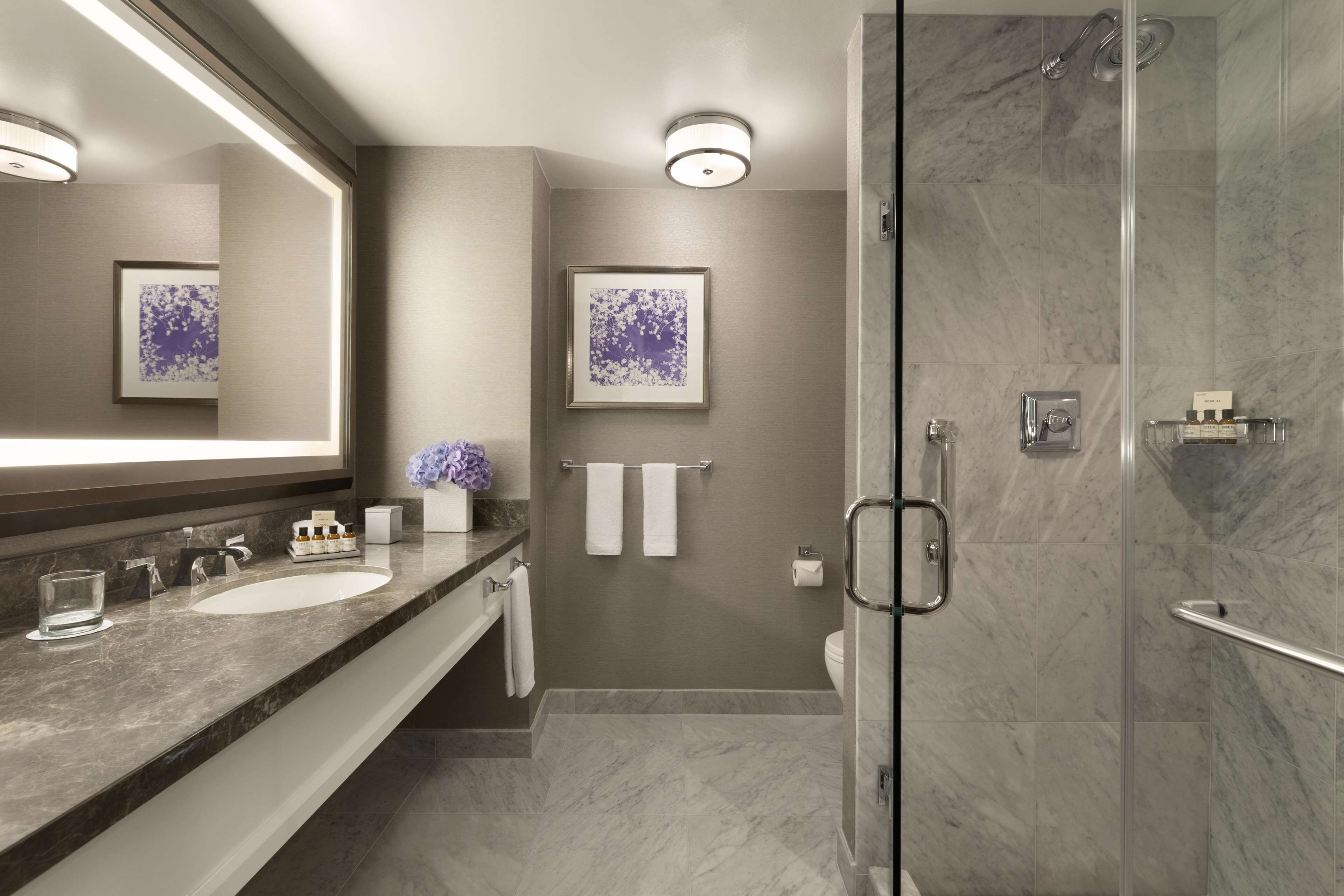 A modern bathroom with a large mirror, two sinks, a shower, and a toilet.