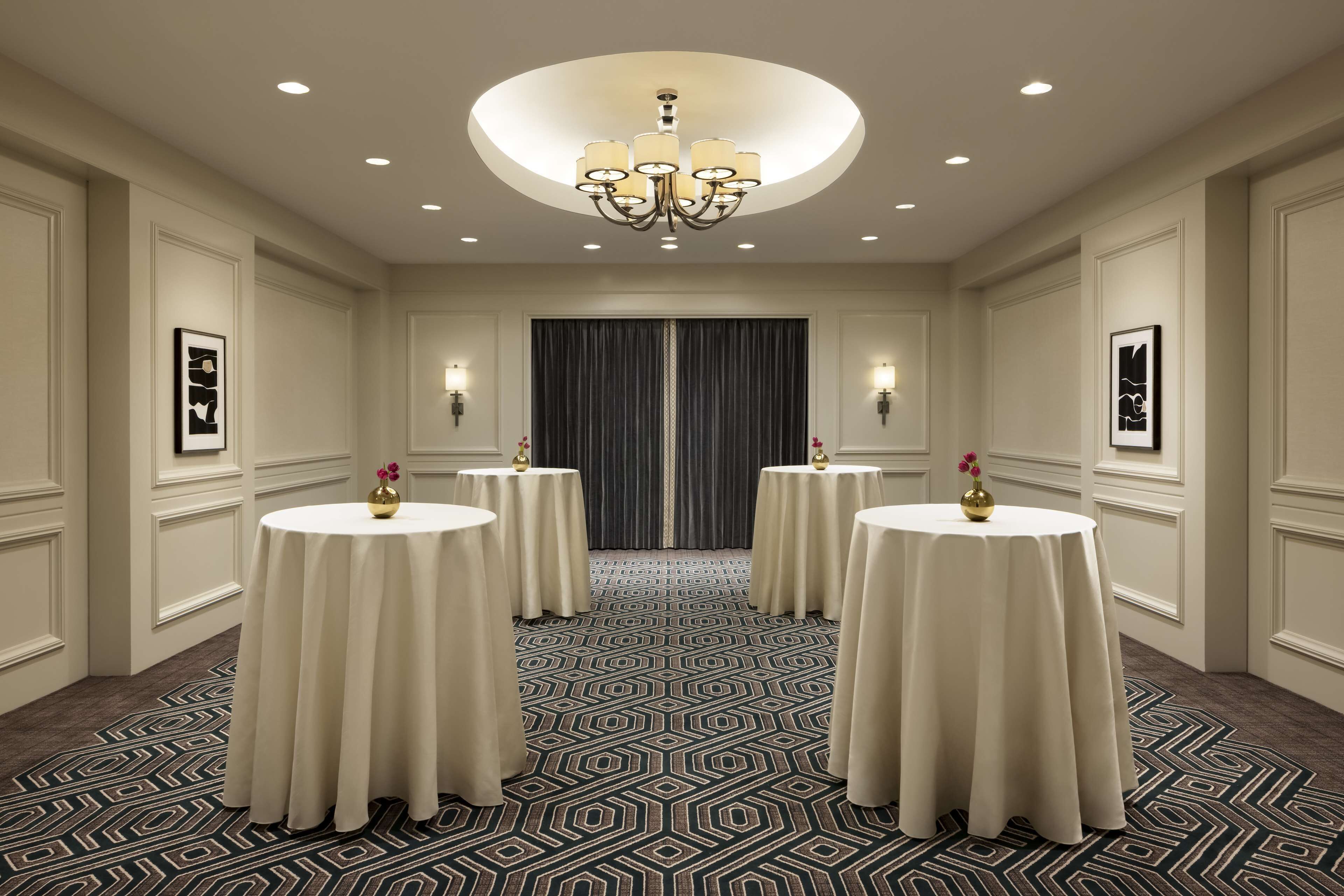 A hotel room with four round tables, a chandelier, and a patterned carpet.