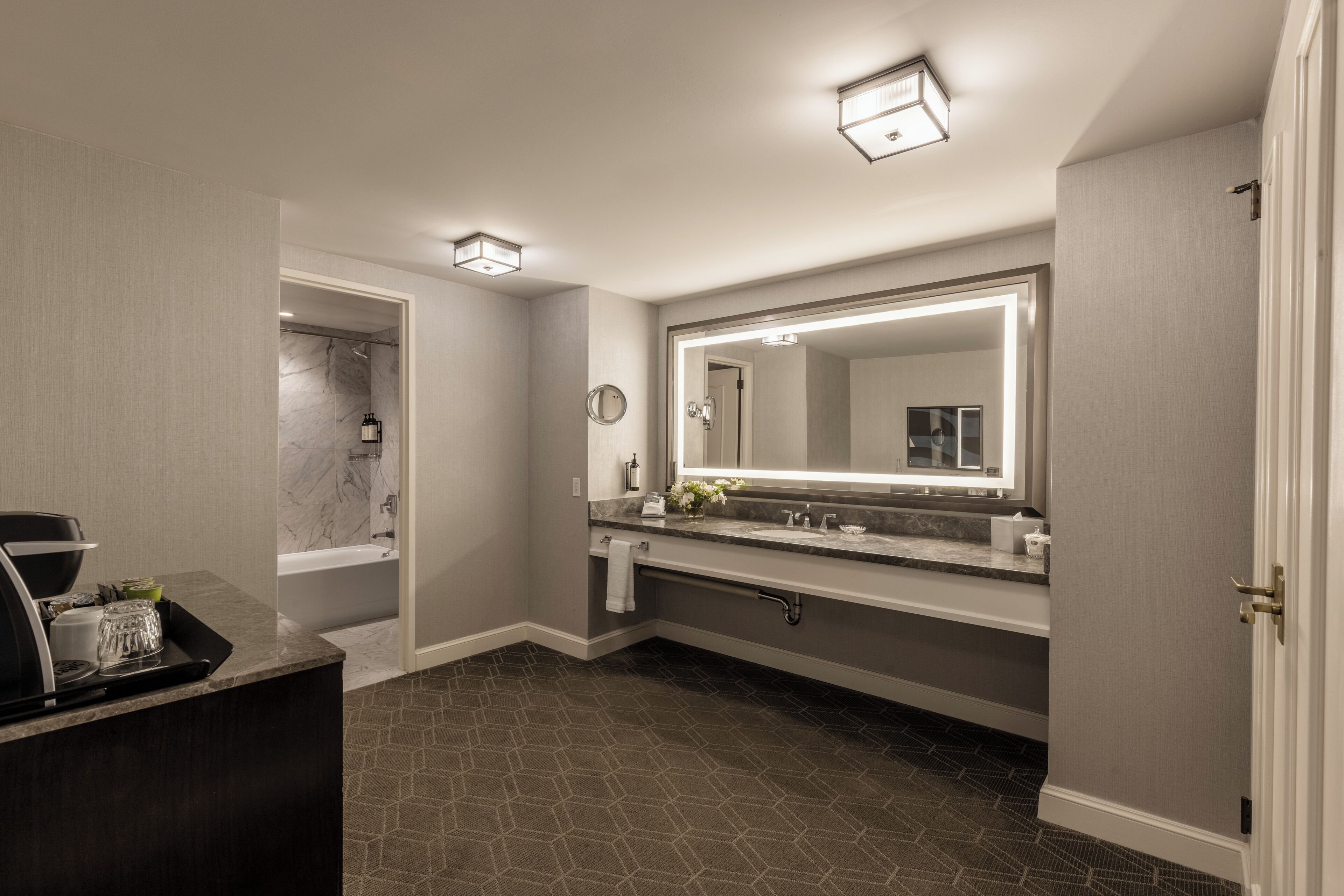 A modern bathroom with a large mirror, a bathtub, and a vanity with a tray of toiletries.