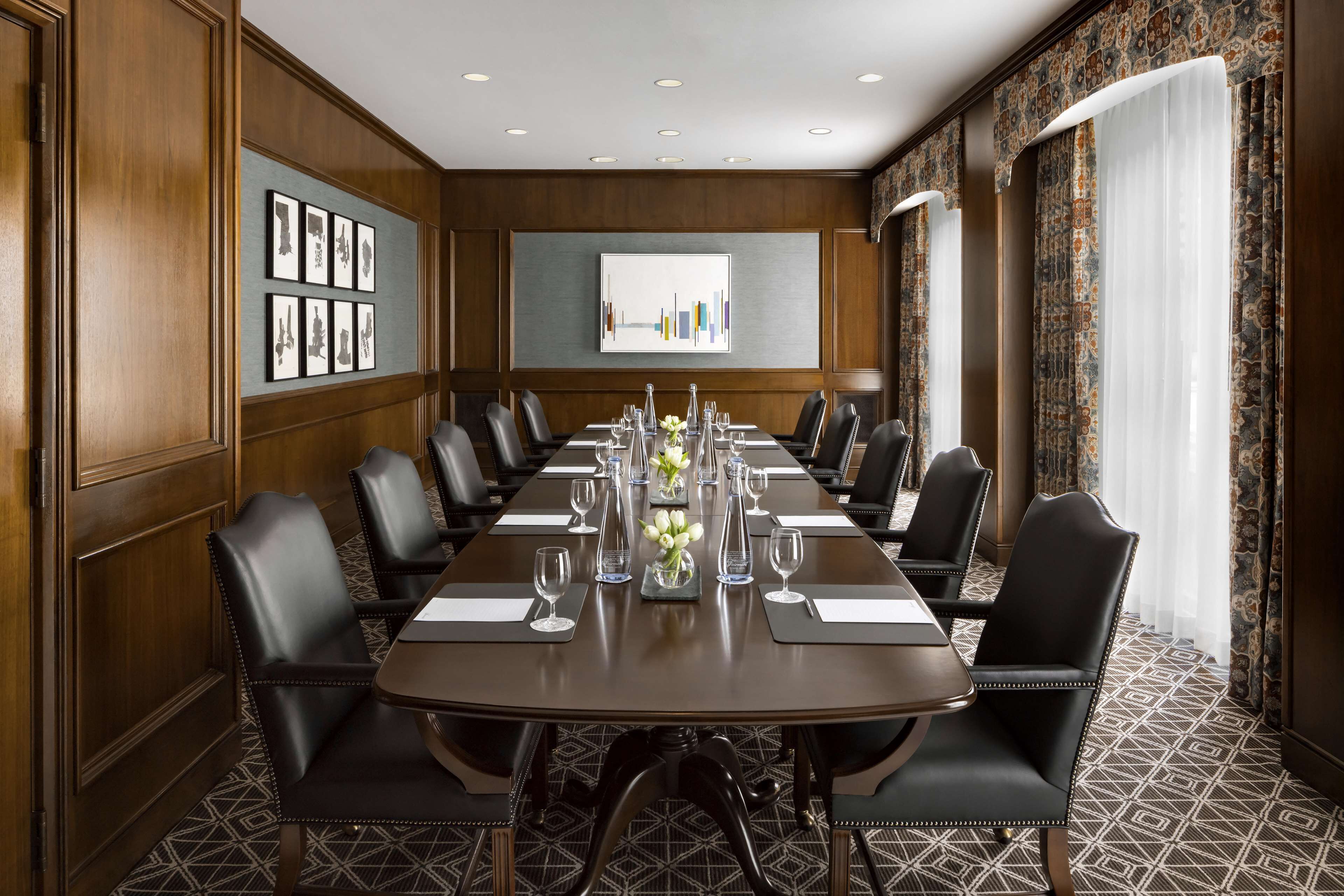 A conference room with a long table, black leather chairs, and a patterned carpet.