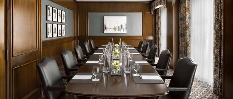 A conference room with a long table, black leather chairs, and a patterned carpet.