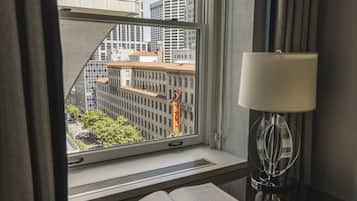 A hotel room with a window view of a cityscape, a lamp, and a book on the windowsill.