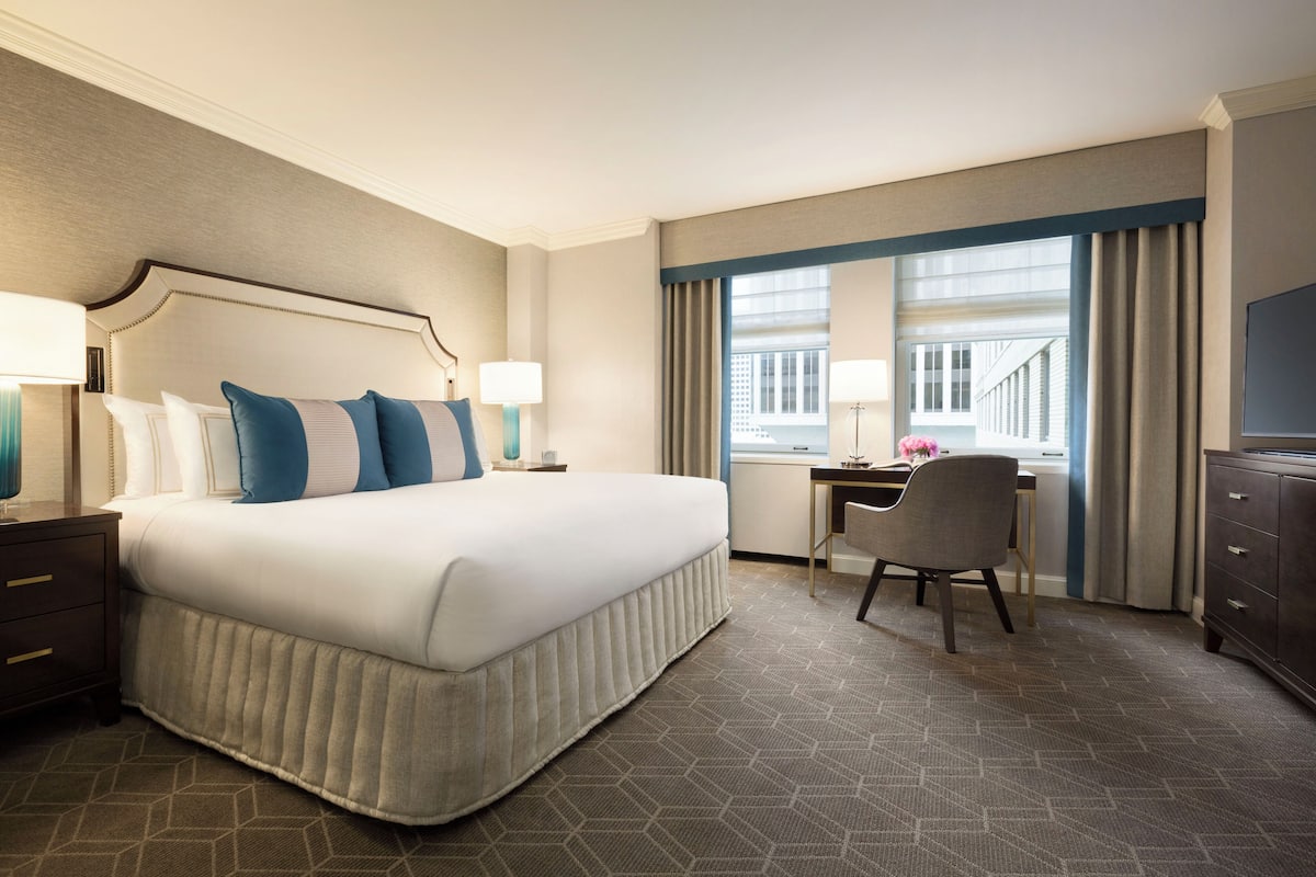 A hotel room with a large bed, a desk, a chair, and a TV.