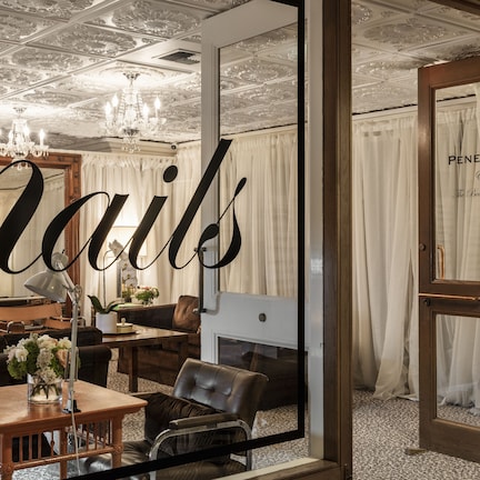 A room with a large mirror, a chandelier, a fireplace, and a door labeled "Penelope The Beauty Bar".
