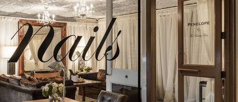 Una stanza con un grande specchio, un lampadario, un camino e una porta con l'insegna 'Penelope The Beauty Bar'.
