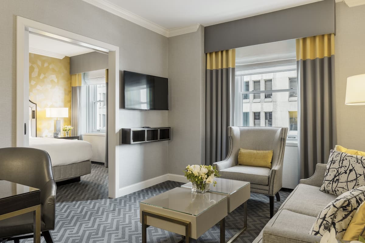 A hotel room with a bed, a sofa, a TV, a coffee table, and a window with curtains.