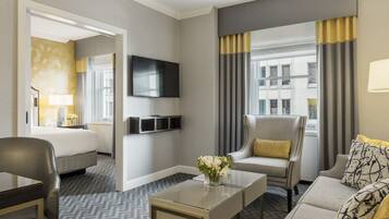 Una habitación de hotel con cama, sofá, televisor, mesa de centro y ventana con cortinas.