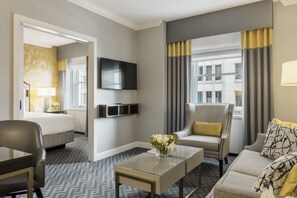 A hotel room with a bed, a sofa, a TV, a coffee table, and a window with curtains.