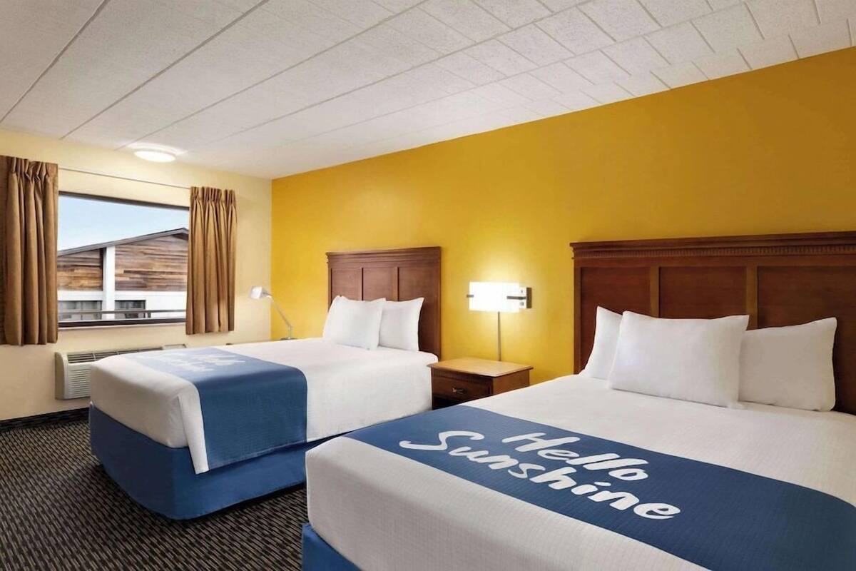 Habitación de hotel con dos camas, una ventana con cortinas, una mesita de noche y una lámpara.
